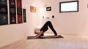 Un tappetino da yoga sul pavimento, con una persona che esegue una posa yoga. Sono presenti striscioni con scritte sulla parete.