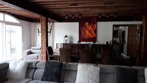A modern living room with a grey sectional sofa, wooden ceiling beams, and a dining area with wooden furniture. - Chambre d'Hôtes La Bastide de Villenave (Villenave)