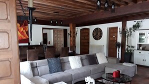 A spacious living room with a large grey sectional sofa, a round coffee table, and a dining area with wooden chairs and a table. - Chambre d'Hôtes La Bastide de Villenave (Villenave)