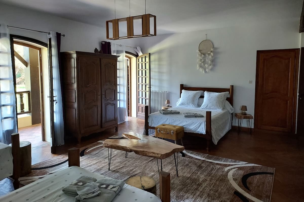 Een slaapkamer met een bed, houten meubels, een hanglamp en uitzicht door een open deur.