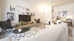 A modern living room with a flat-screen TV, a coffee table, a sofa, and a dining area with a lamp. - Chez Meredith (Brussels)