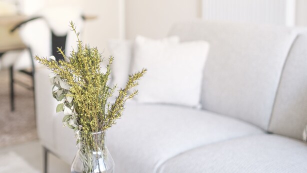 A modern living room with a white sofa, a round black coffee table with two white candles, and a vase with dried flowers. - Chez Meredith (Brussels)