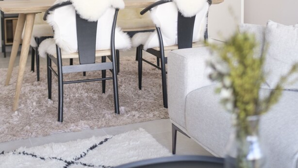 Ein moderner Essbereich mit einem Holztisch, Stühlen mit Felldecken und Pendelleuchten.