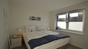 Ein Schlafzimmer mit Bett, Nachttisch, Nachttischlampe, Fenster und Heizkörper.