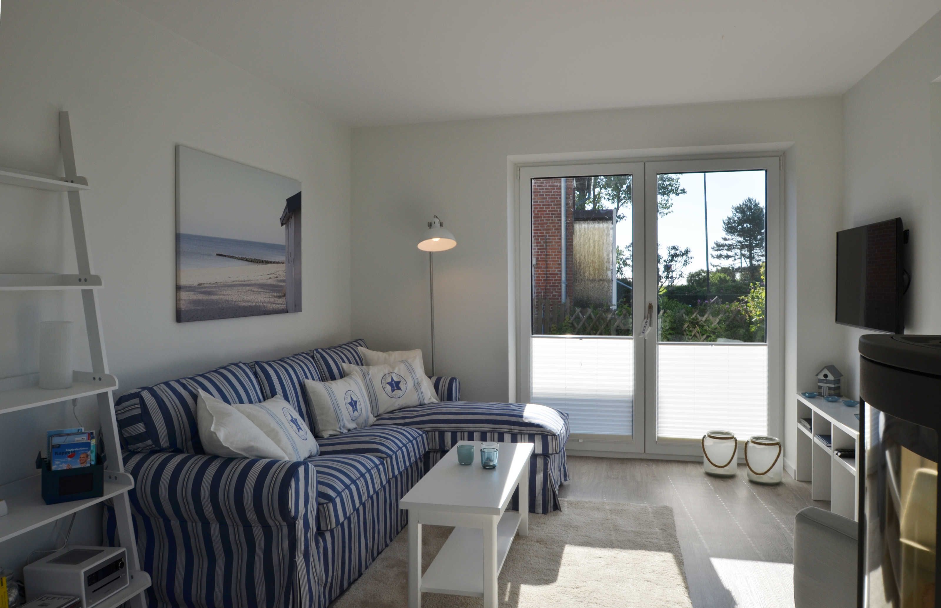 Una sala de estar moderna con un sofá a rayas, una mesa de centro blanca, un televisor de pantalla plana y un ventanal con vistas al exterior.