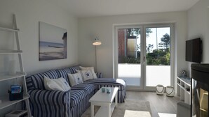 Ein modernes Wohnzimmer mit einem gestreiften Sofa, einem weißen Couchtisch, einem Flachbildfernseher und einem großen Fenster mit Blick ins Freie.