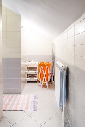 A small, bright bathroom with white tiles, a white radiator, a white shelf unit, and a striped rug.