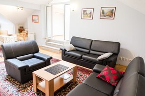 A modern living room with a sofa, armchairs, and a coffee table. There is a dining area visible in the background.