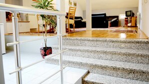 Escadaria que leva a uma sala de estar com sofá, TV e uma planta.