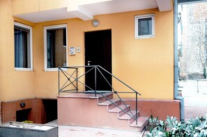 A building with a yellow exterior, a staircase with metal railings, and a door leading to an interior space.