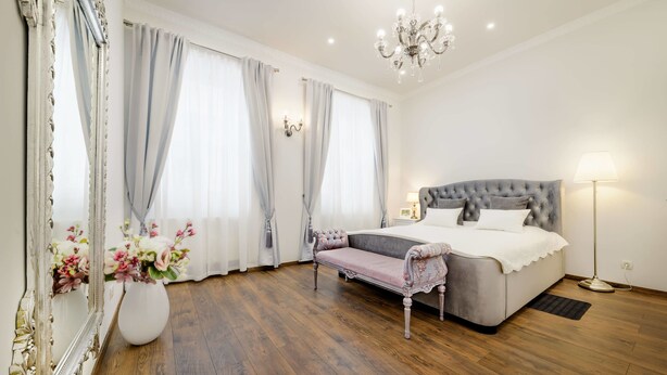 A bedroom with a large bed, a bedside table, a floor lamp, a mirror, and a vase with flowers. - Royal Apartment Zagreb (Zagreb)
