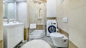 Un baño moderno con ducha de vidrio, lavadora integrada, inodoro y lavabo con espejo.