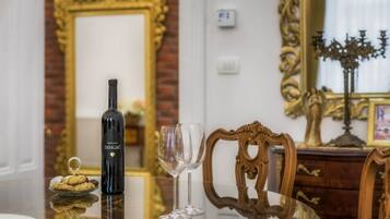 A bottle of Madirazza DINGAČ wine, a glass, and a plate with cookies on a reflective table in a room with ornate furniture and a mirror.