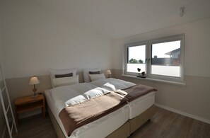 Ein Schlafzimmer mit einem Bett, einem Nachttisch, einem Fenster und Blick ins Freie.
