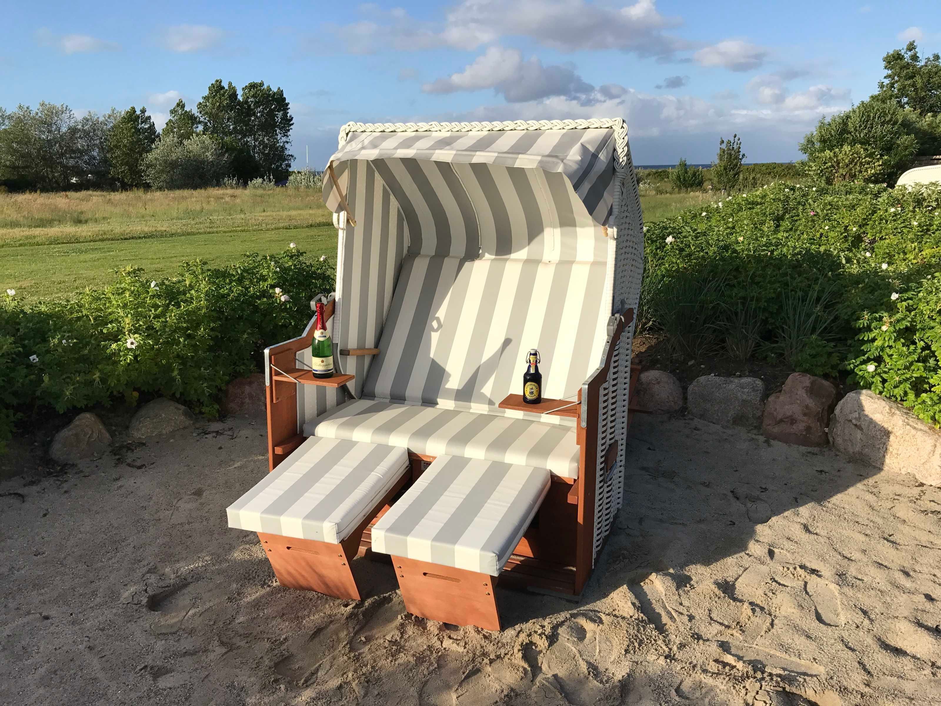 Une chaise de plage avec un parasol à rayures, deux bouteilles de boissons et une petite table.