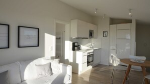 Une cuisine moderne avec des meubles blancs, un four encastré et un four à micro-ondes. On y trouve également un coin repas avec une table et des chaises en bois.