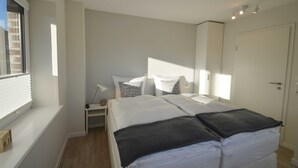Une chambre à coucher avec un grand lit, une table de chevet, une commode, une fenêtre et une porte.