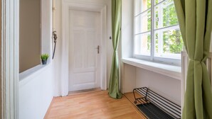 Un couloir avec une porte blanche, une fenêtre ornée de rideaux verts et un plancher en bois.