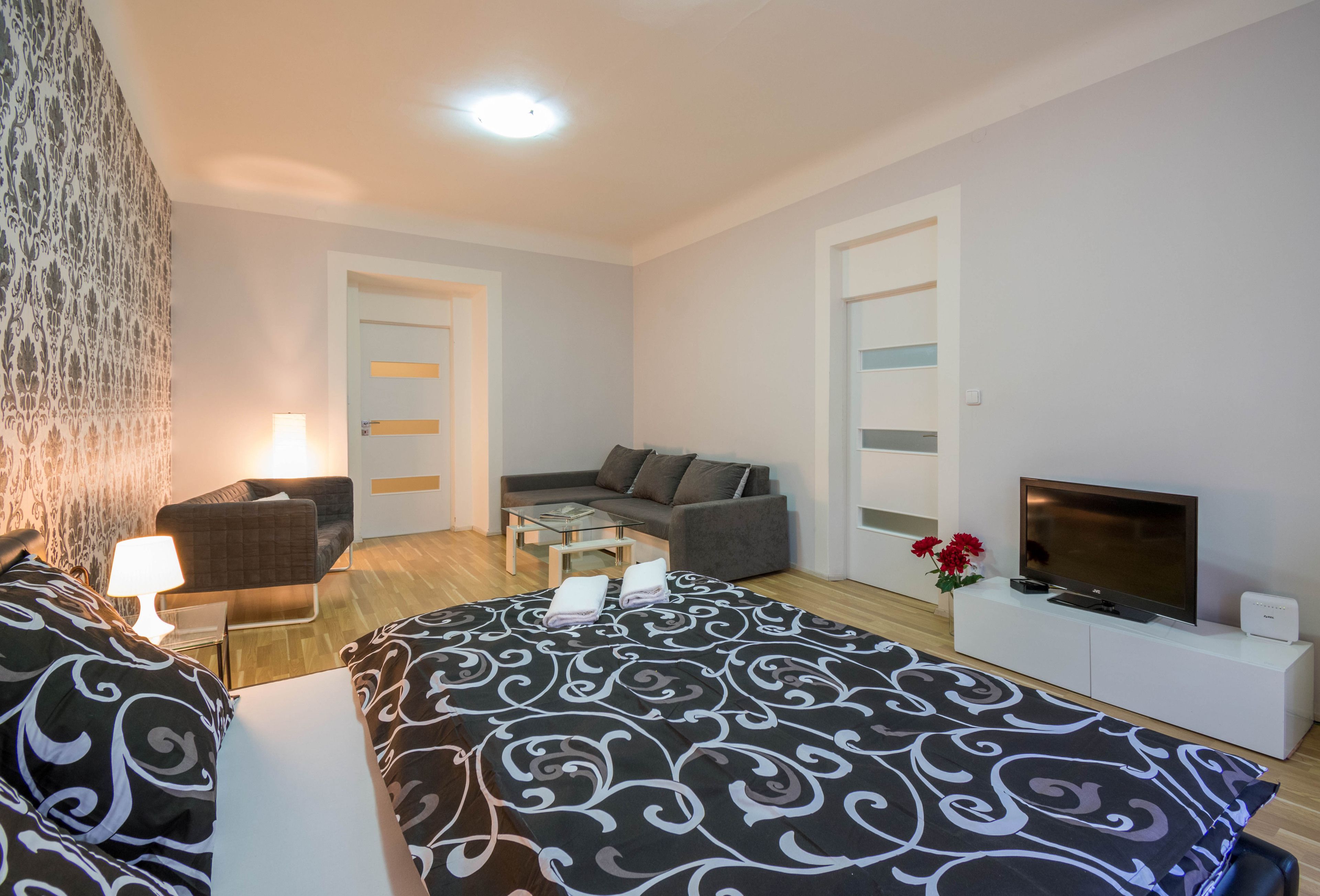 A modern hotel room with a large bed, a sofa, a TV, and a small table.
