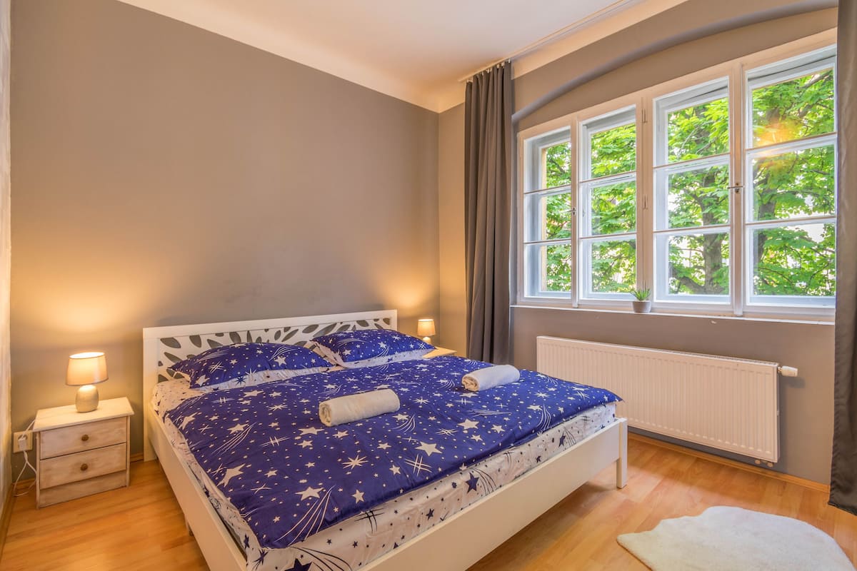 Ein Schlafzimmer mit Bett, Nachttisch, Fenster und Heizkörper.
