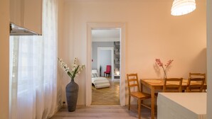 Un couloir mène à une salle à manger où se trouvent une table et des chaises, un vase avec des fleurs et un radiateur.