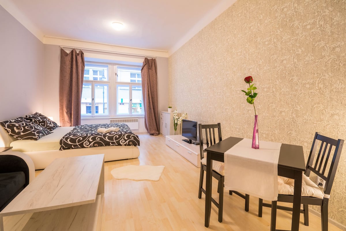 Ein modernes Wohnzimmer mit einer Couch, einem Esstisch mit Stühlen, einem Fernseher und einem Fenster mit Vorhängen.