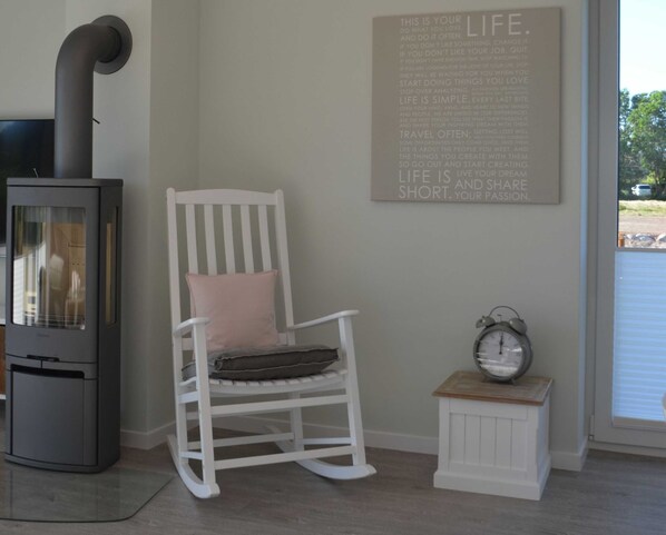 Una habitación con una mecedora blanca, una pequeña mesa blanca con un reloj y una chimenea gris.