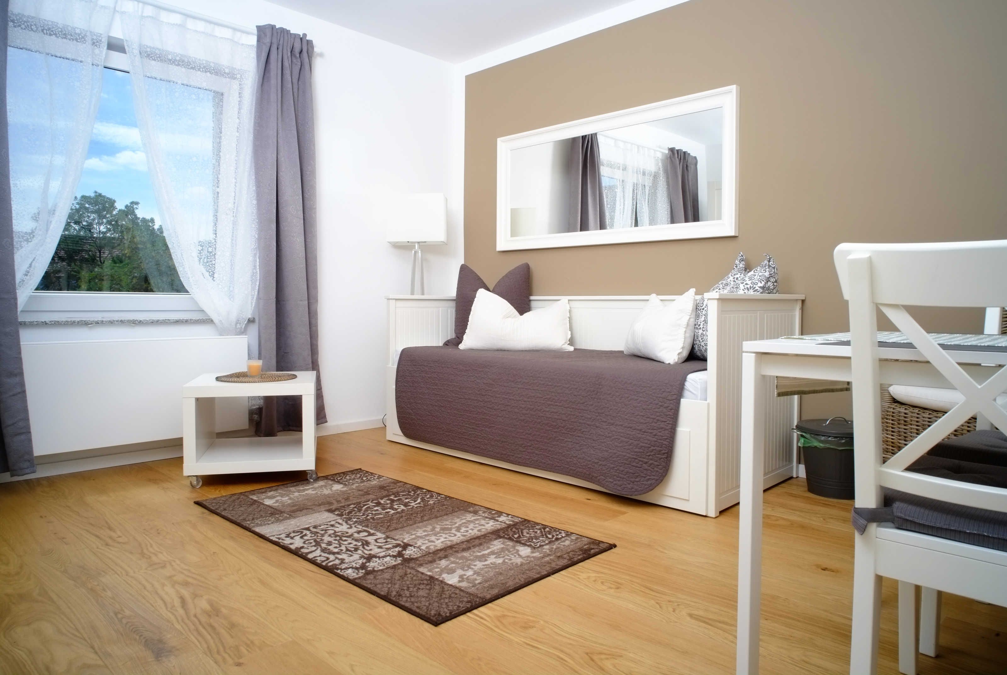 Une chambre à coucher avec un lit, une table de chevet, une lampe et une vue sur les arbres par la fenêtre.