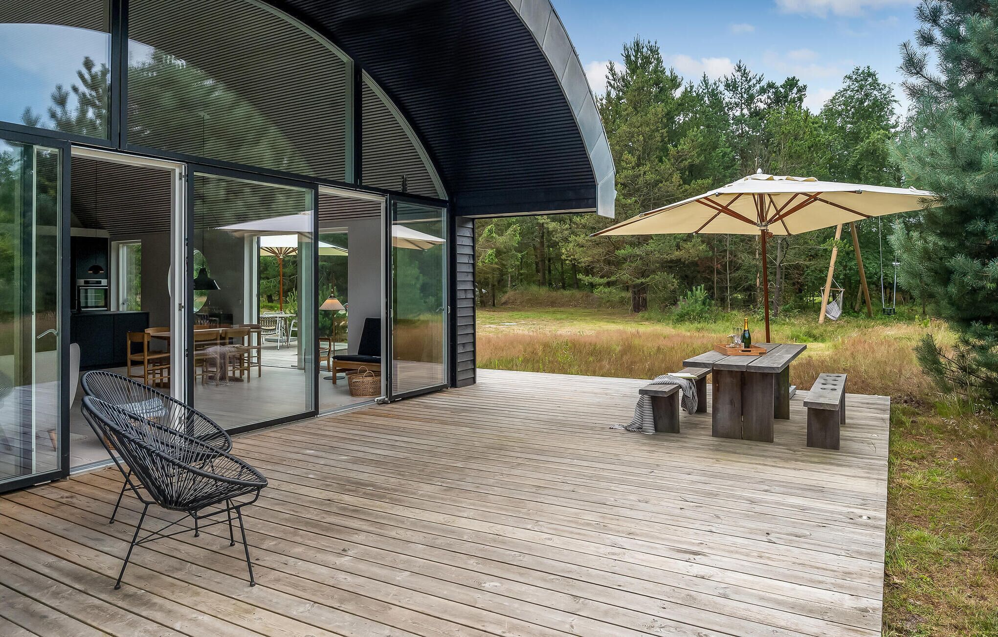 A modern outdoor deck with a glass-enclosed patio, wooden furniture, and a large umbrella.