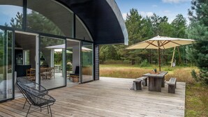 A modern outdoor deck with a glass-enclosed patio, wooden furniture, and a large umbrella. - 2 bedroom amazing home in Vig (Vig)