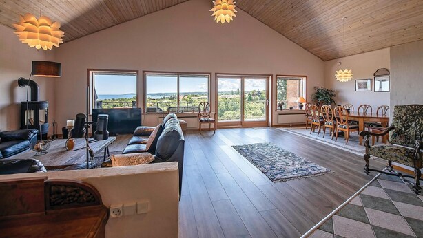 A spacious living room with a large wooden ceiling, a cozy fireplace, and a view of the countryside through large windows.