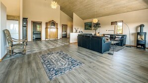 A spacious living area with a high ceiling, a large wooden cabinet, a black sofa, a patterned rug, and a wood-burning stove.