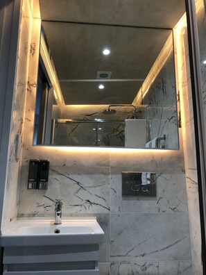 Une salle de bain moderne avec un lavabo en marbre, une douchette à main et un miroir encastré.