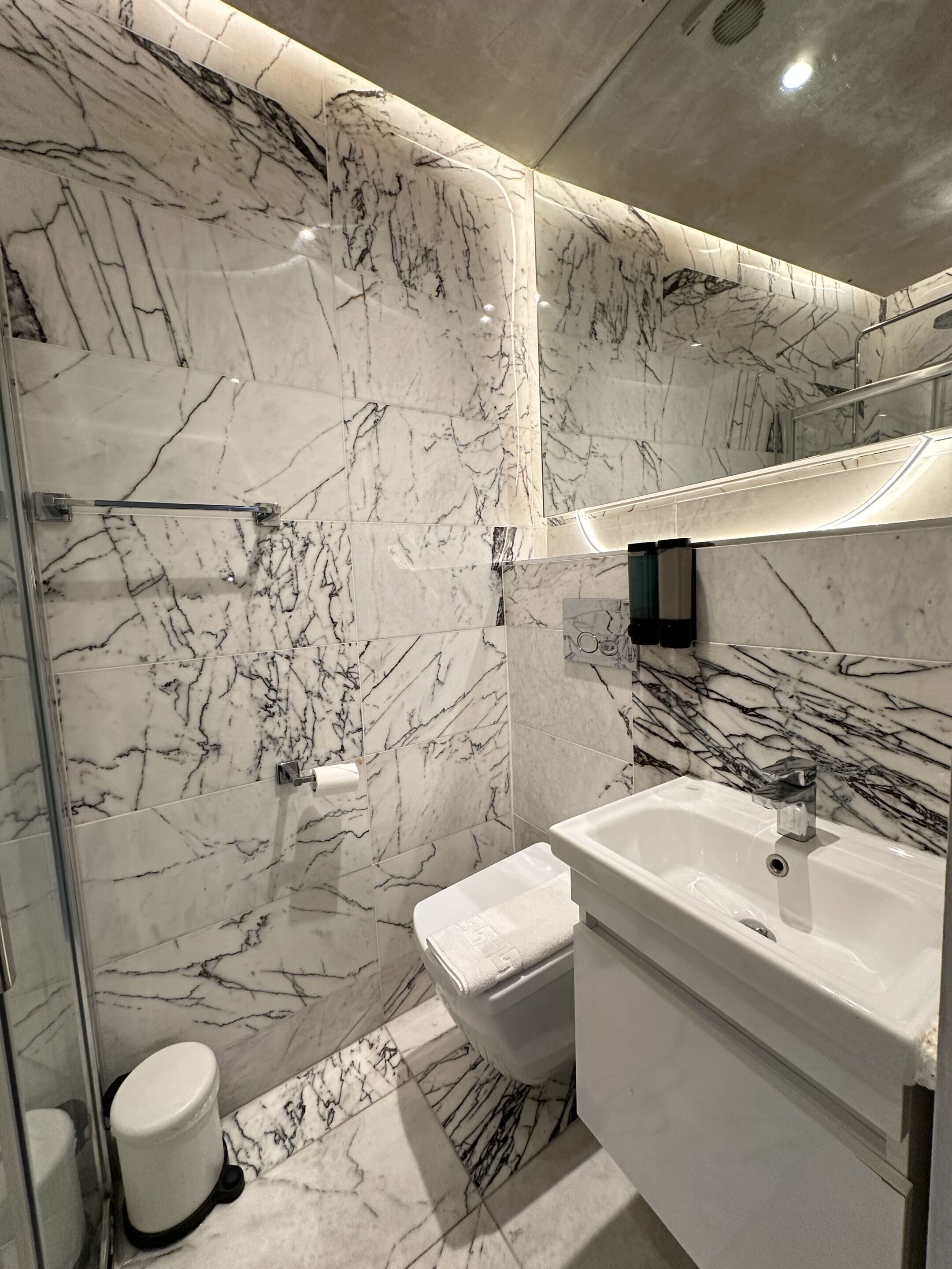 Un baño con paredes de mármol y un lavamanos blanco.