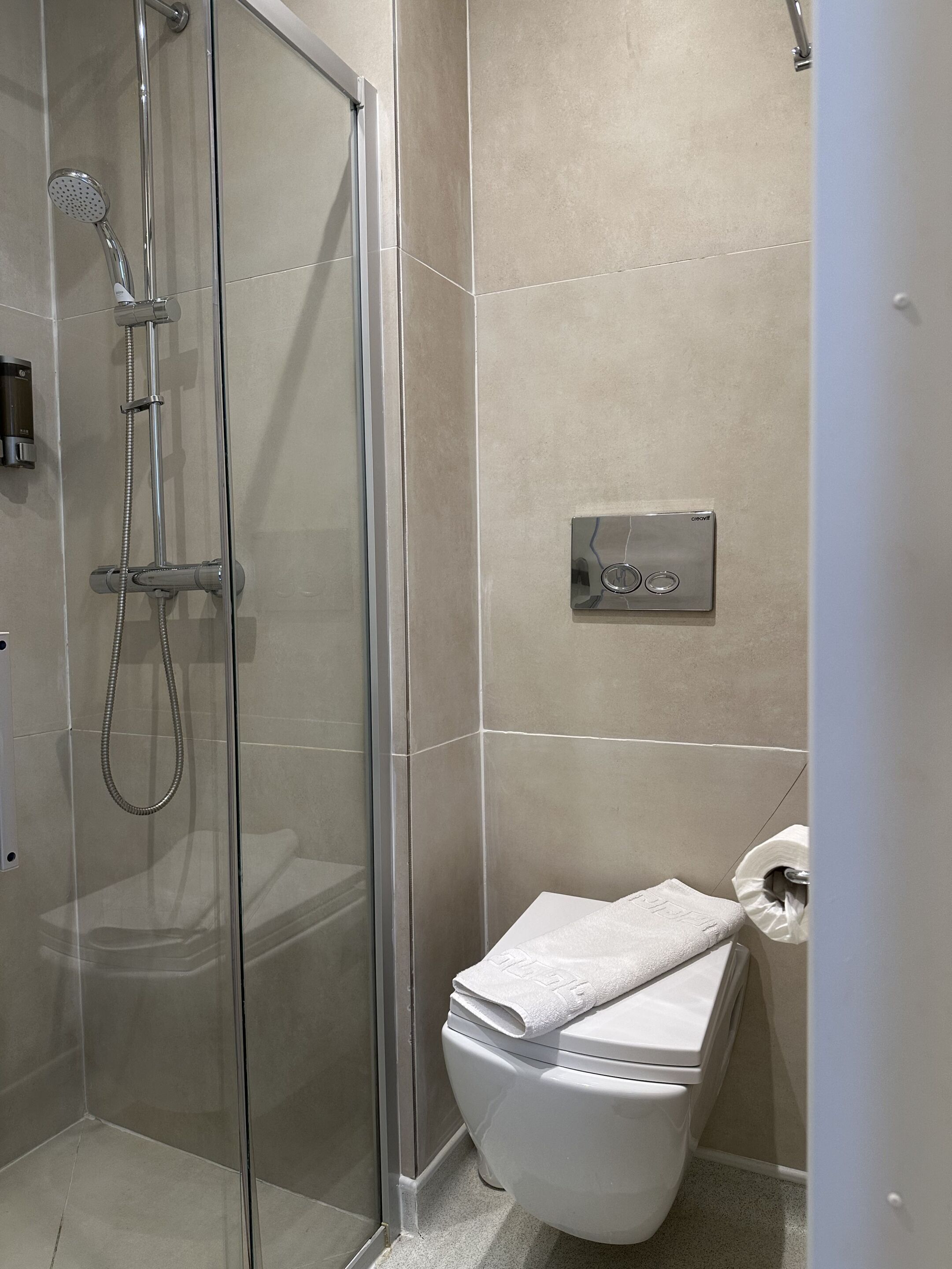 A bathroom with a glass-enclosed shower, a toilet, and a towel rack.