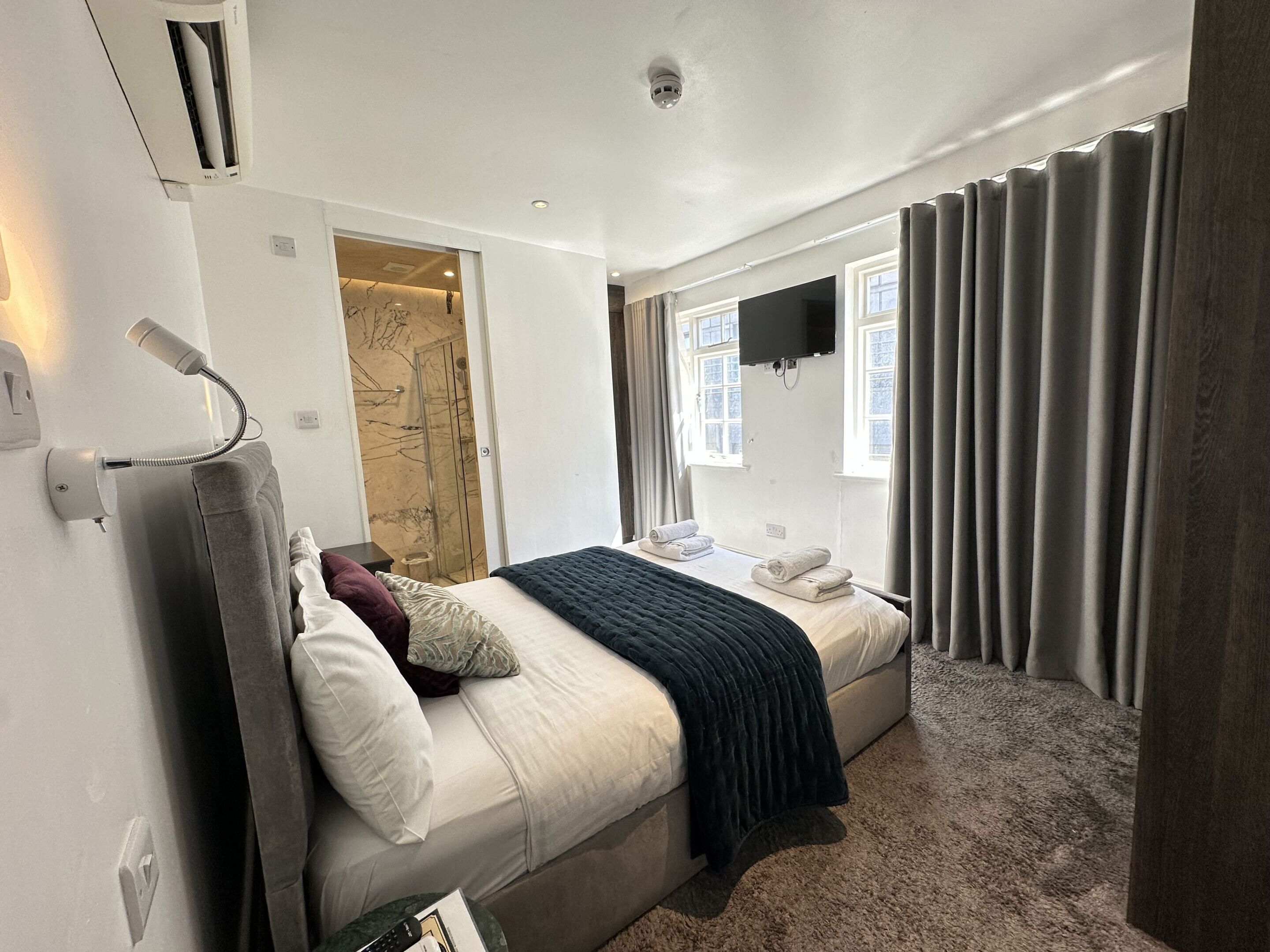 A modern bedroom with a bed, a bedside table, a wall-mounted TV, and a window with curtains.