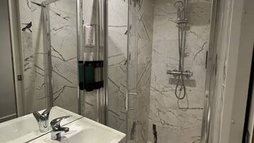 Un baño con ducha de vidrio, un lavamanos blanco con grifo cromado y paredes con diseño de mármol.
