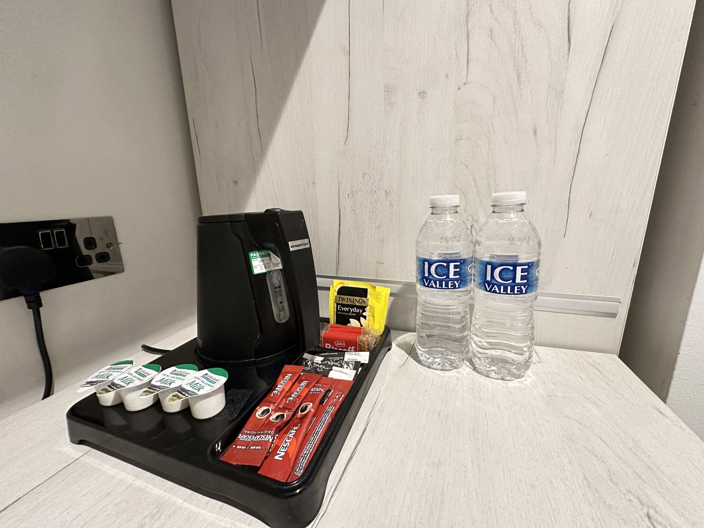Un mini-bar dans la chambre d’hôtel, comprenant une machine à café, des bouteilles d’eau et diverses collations.