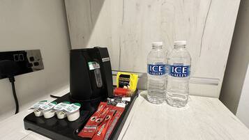 Un mini-bar dans la chambre d’hôtel, comprenant une machine à café, des bouteilles d’eau et diverses collations.