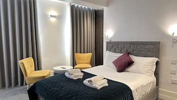Ett hotellrum med en säng, två stolar, ett runt bord och ett stort fönster med gardiner.