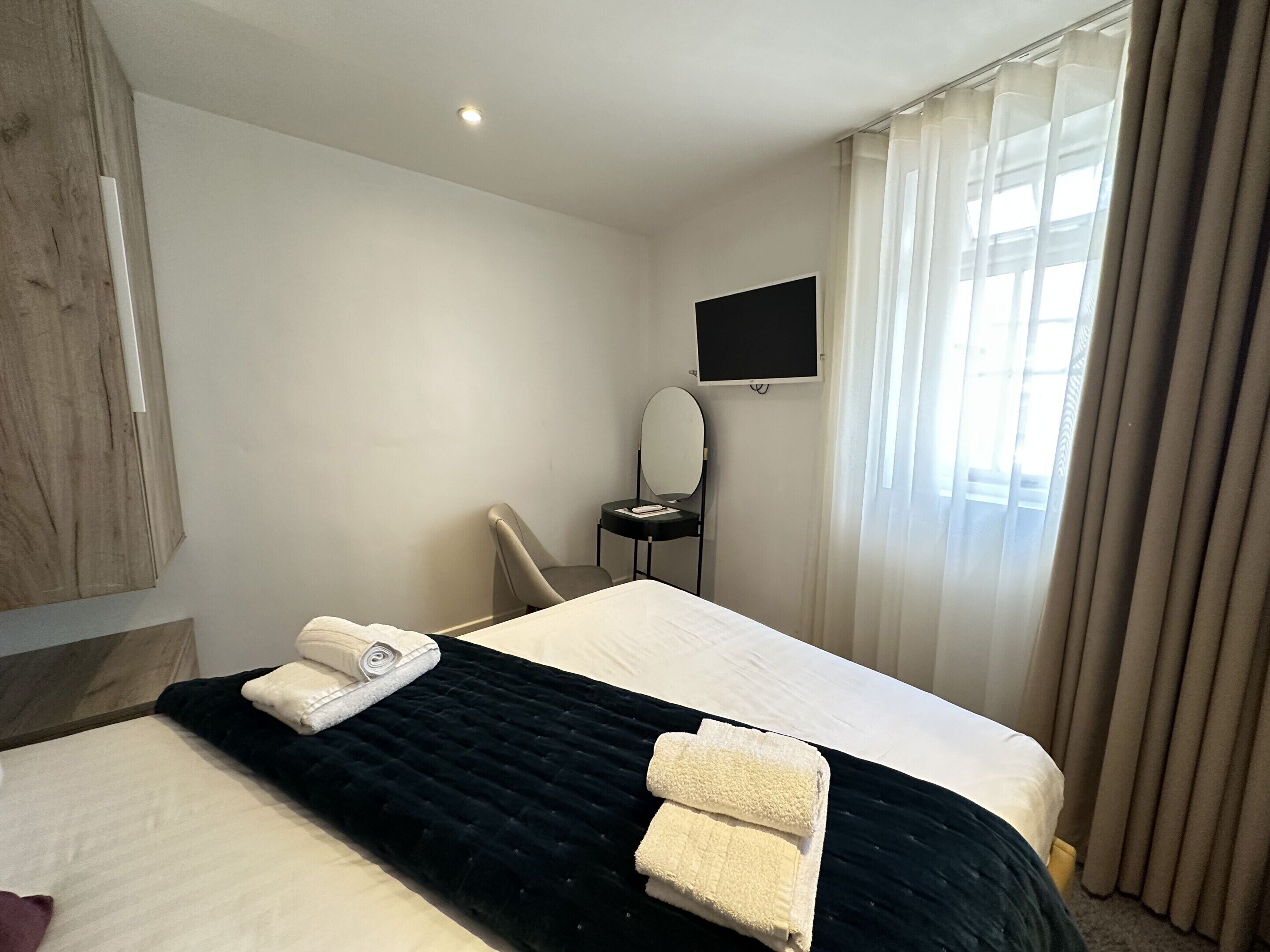Ein Hotelzimmer mit Bett, Sessel, Flachbildfernseher und einem fenster mit Vorhängen.