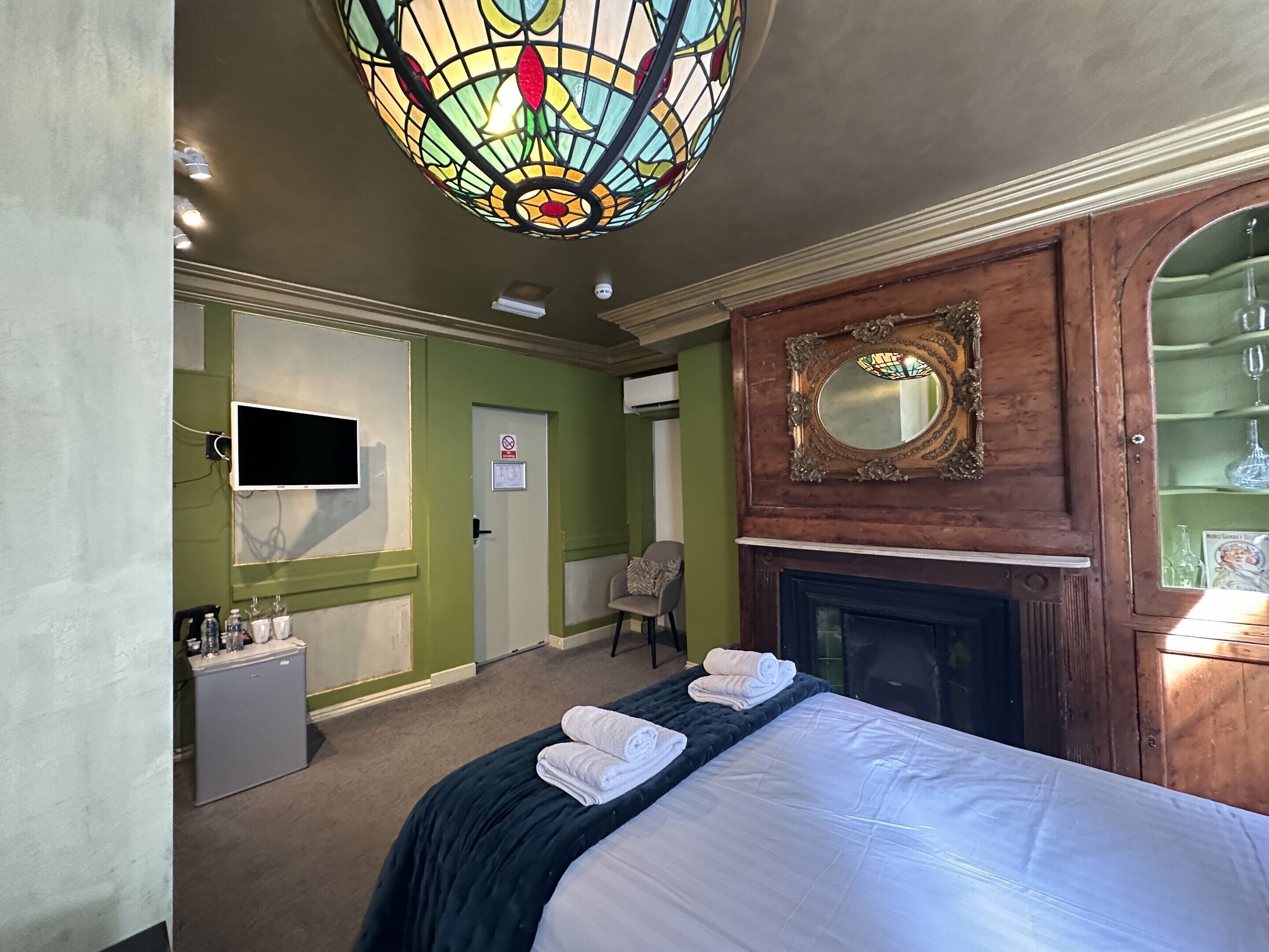 A hotel room with a bed, a television, a fireplace, and a mirror.