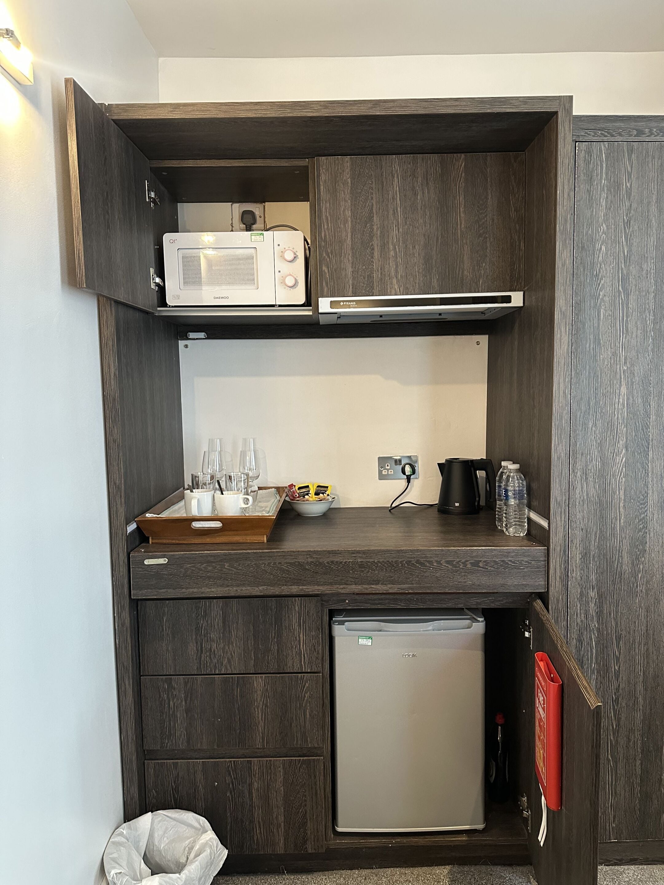 Uma cozinha compacta equipada com micro-ondas, um frigorífico pequeno e uma máquina de café.