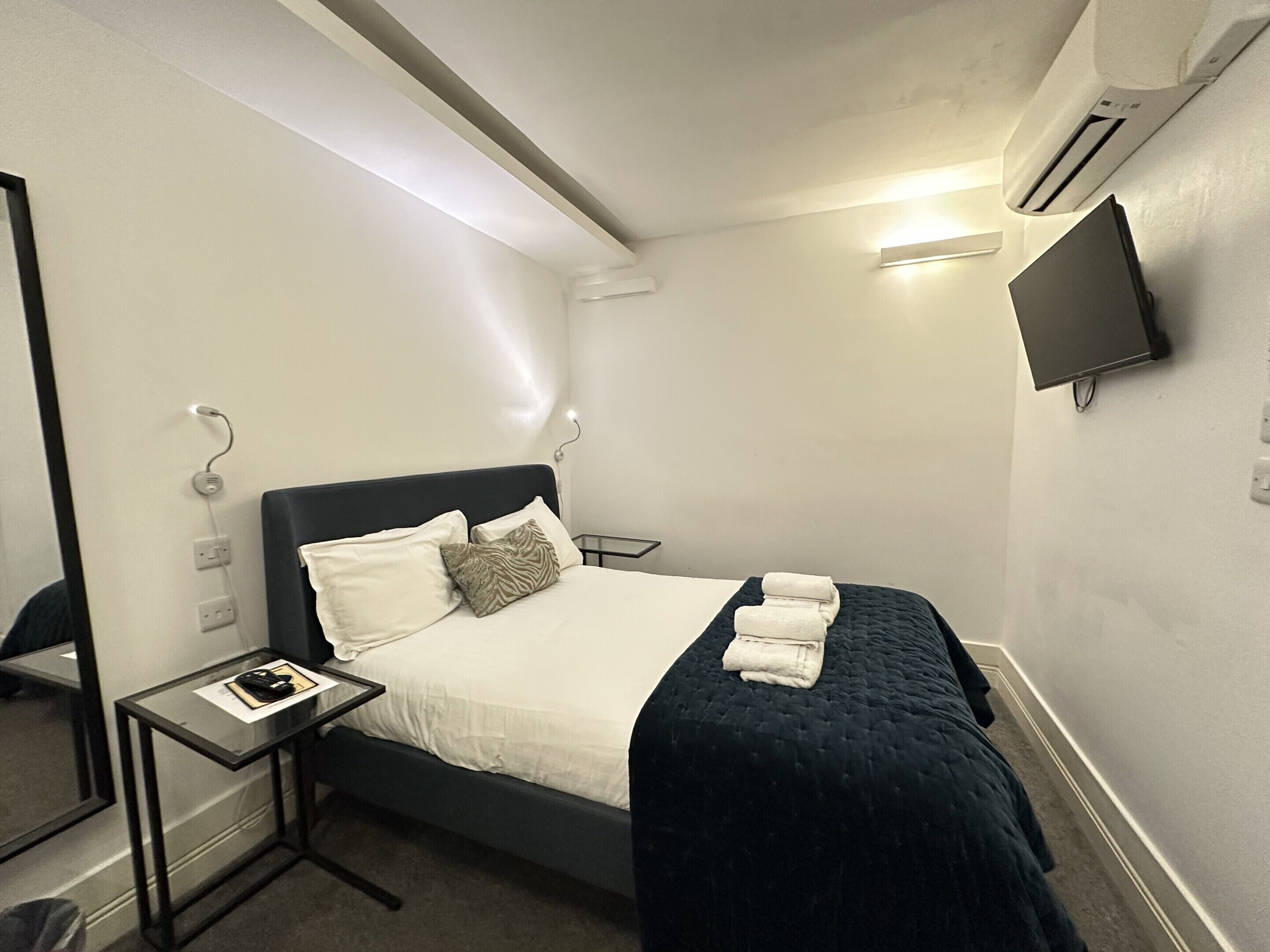 A hotel room with a bed, bedside table, and a flat-screen TV mounted on the wall.