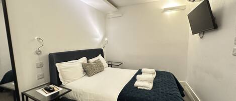 A hotel room with a bed, bedside table, and a flat-screen TV mounted on the wall.