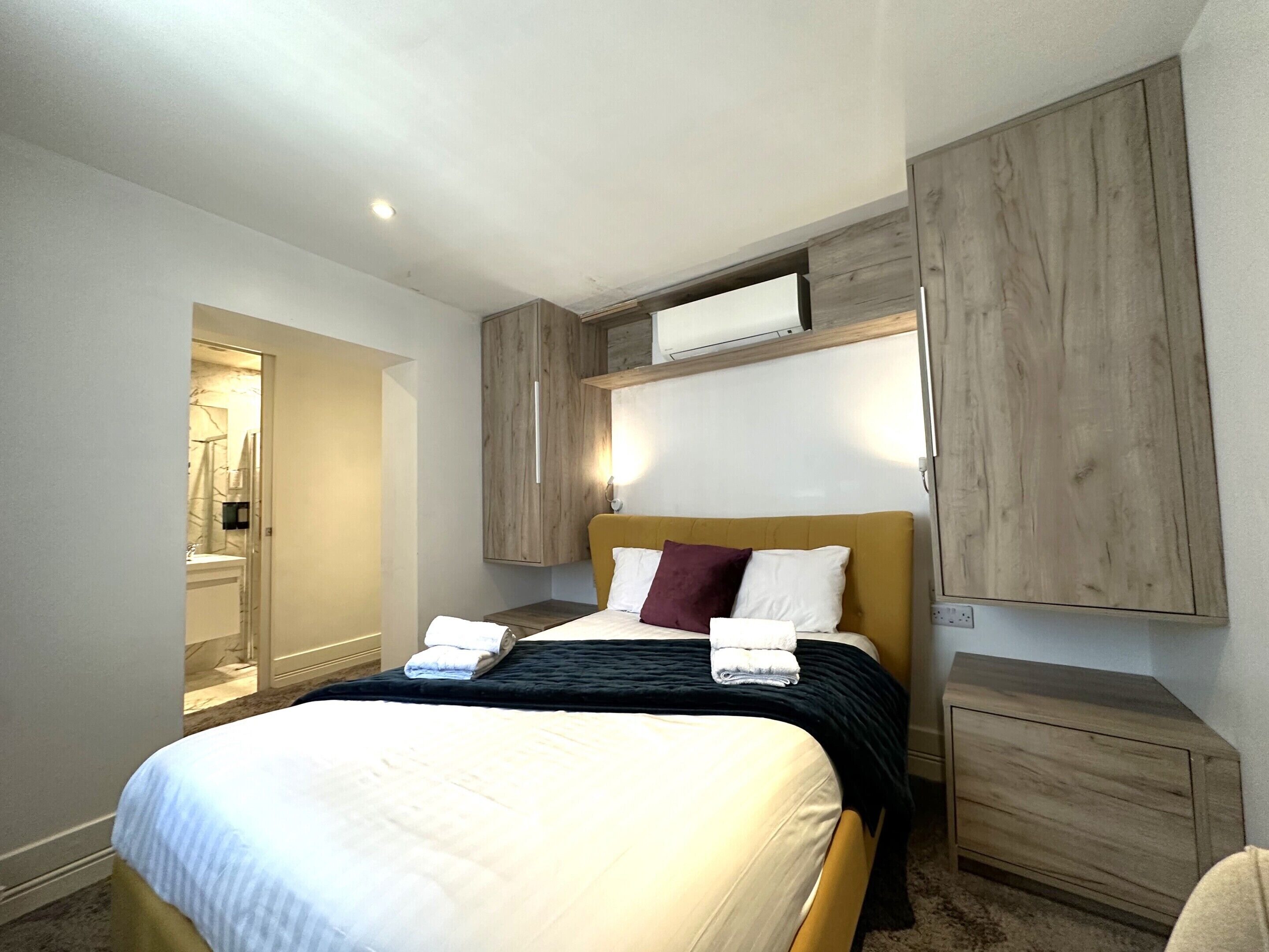 Une chambre d’hôtel avec un lit, une armoire en bois et une salle de bain visible à travers une porte ouverte.