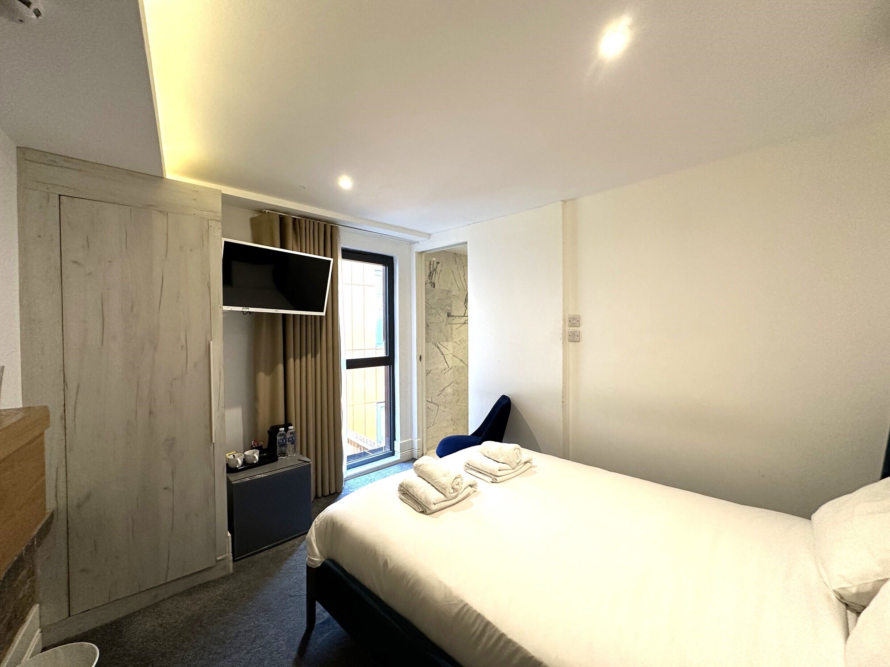 A hotel room with a bed, a TV mounted on the wall, a wardrobe, and a window with curtains.