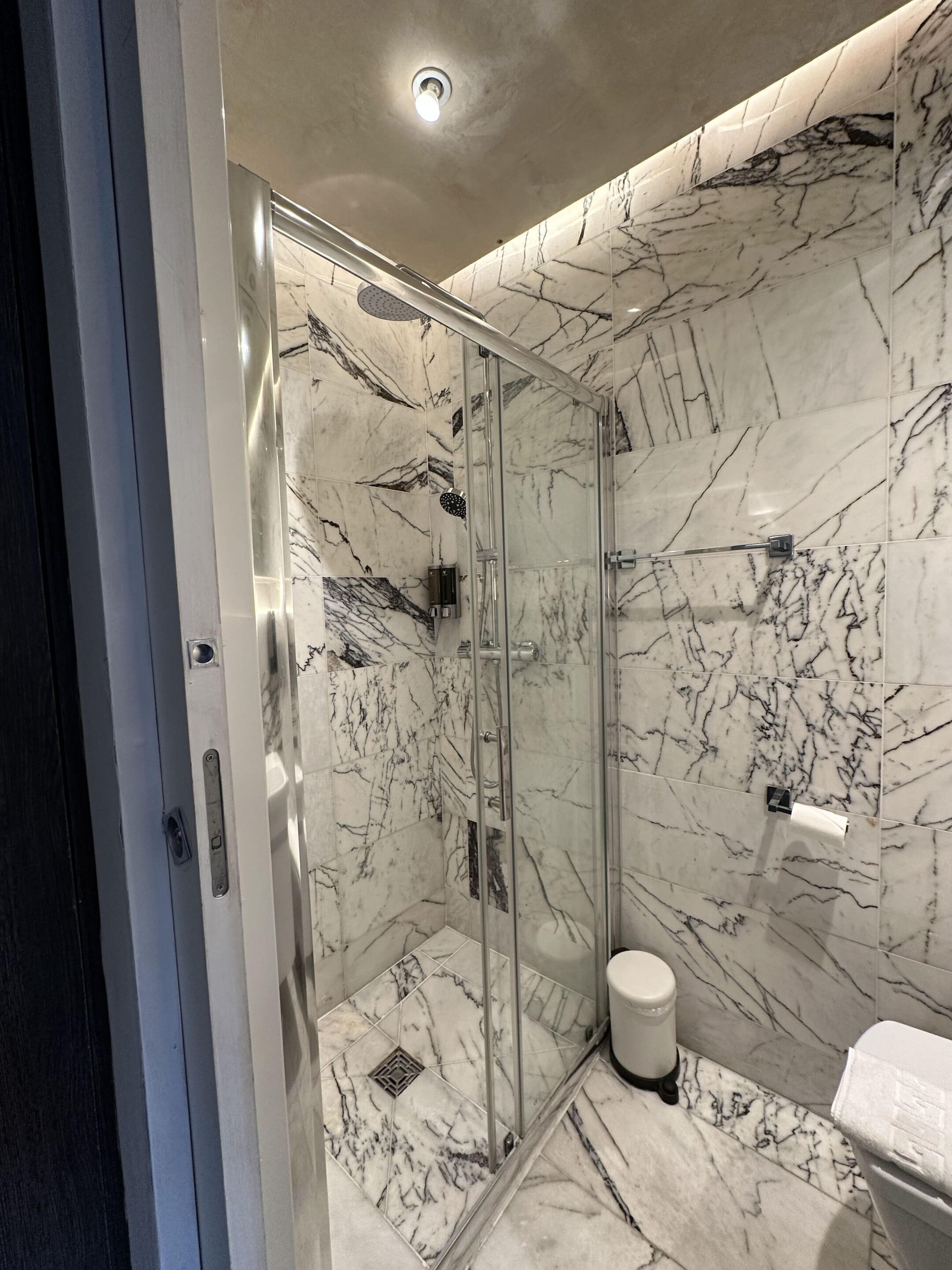 A modern bathroom with a glass-enclosed shower, marble walls, and a toilet.