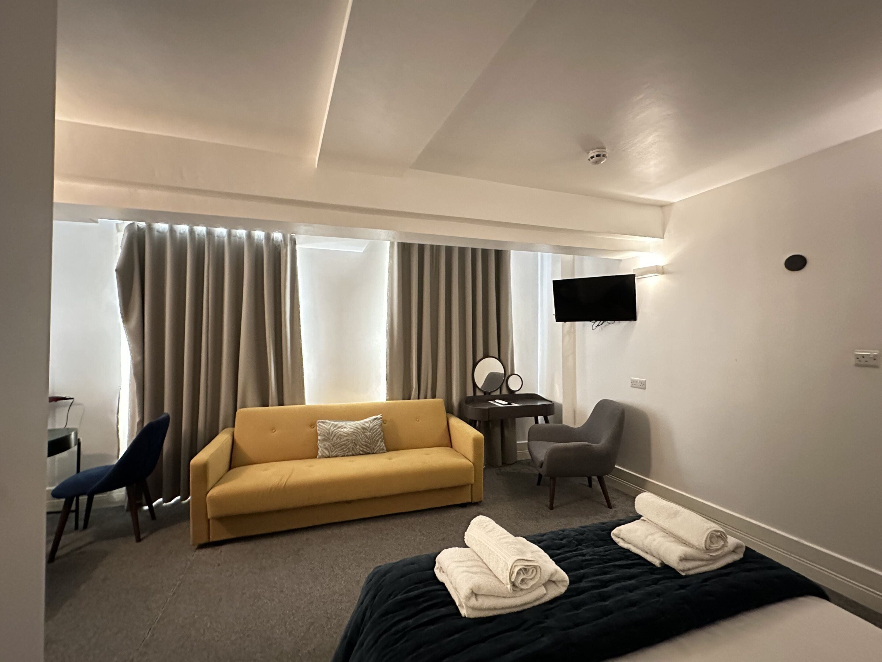 A hotel room with a sofa, a desk with a chair, a TV, and two beds with towels.