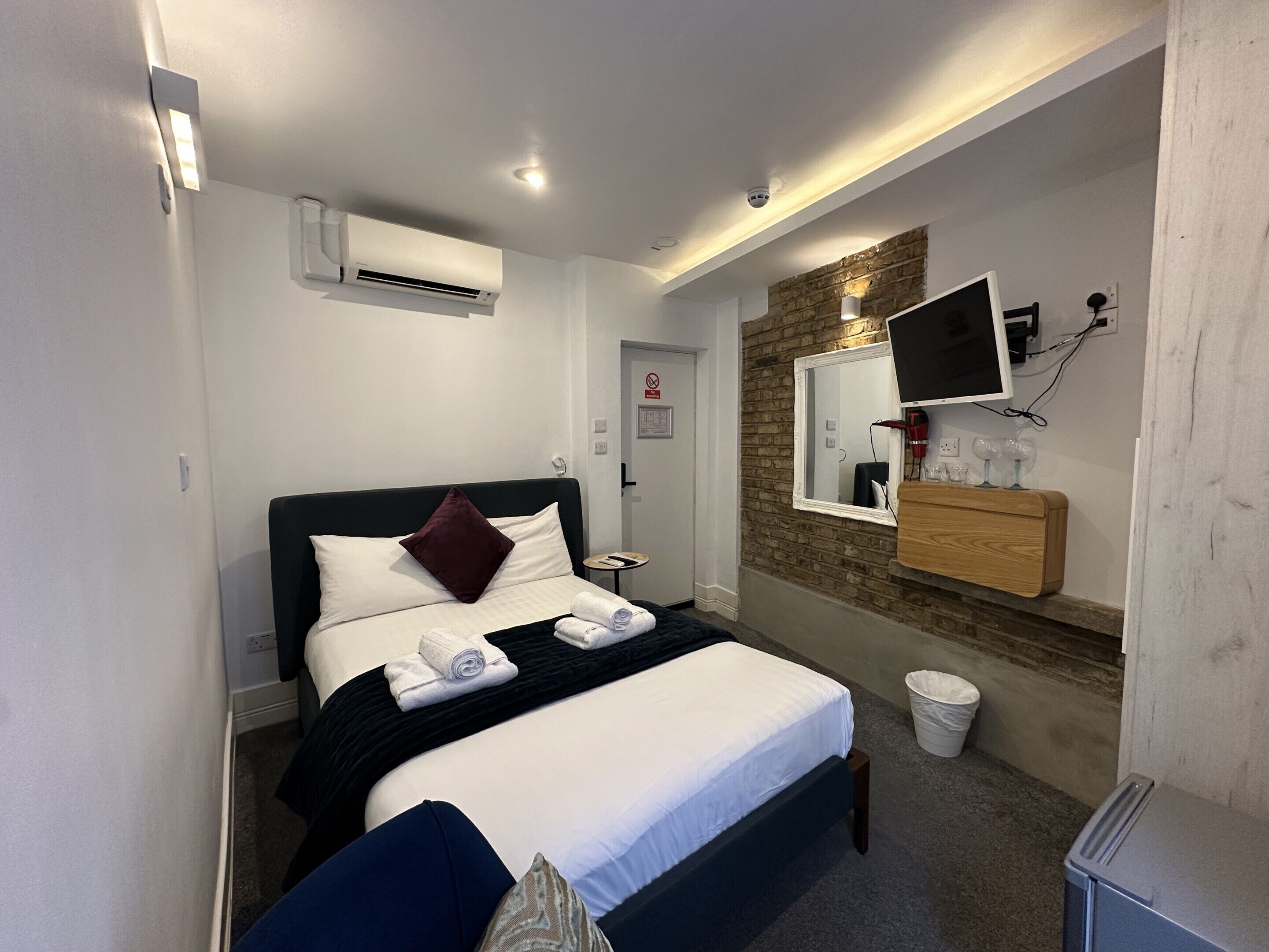 Een hotelkamer met een bed, een tv aan de muur, een klein tafeltje en een afvalbak.